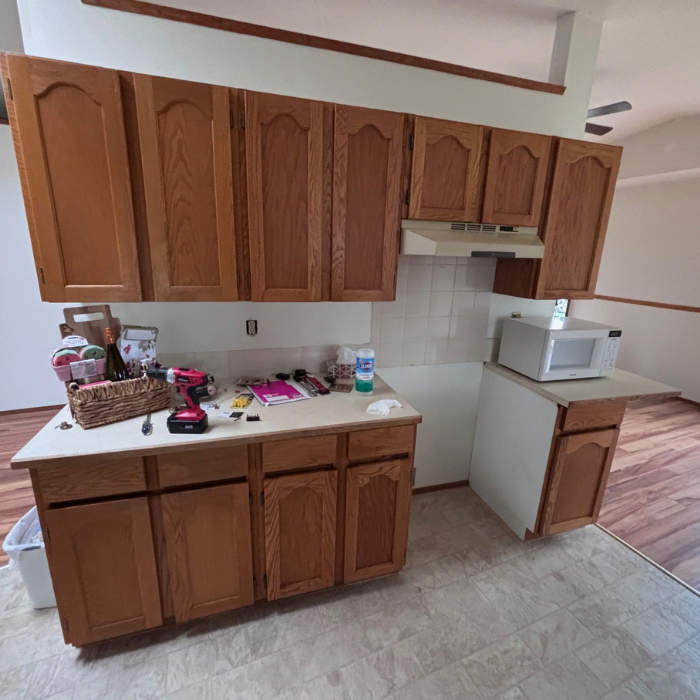 Kitchen with wooden cabinets, two sinks and faucets, and a window above the counter, being remodeled.